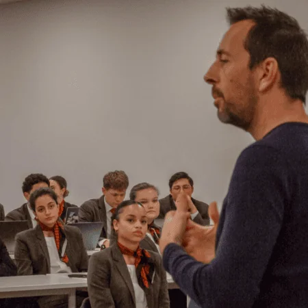 Enseignant donnant un cours devant étudiants en uniforme avec ordinateurs portables.