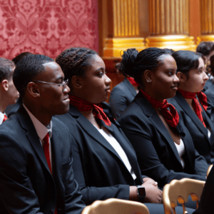 Délégation en costumes formels assise, cravates rouges, alignée dans une salle cérémonielle.