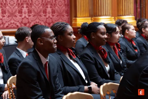 Délégation en costumes formels assise, cravates rouges, alignée dans une salle cérémonielle.
