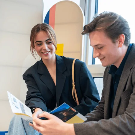 Deux adultes consultent une brochure colorée par lumière naturelle dans un bureau moderne.