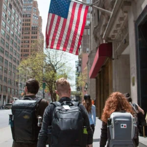 Drapeau am&eacute;ricain au-dessus de pi&eacute;tons avec sacs &agrave; dos dans une rue de centre-ville.