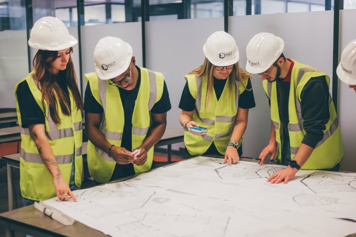 Équipe de chantier en gilets et casques examinant plans techniques sur table.