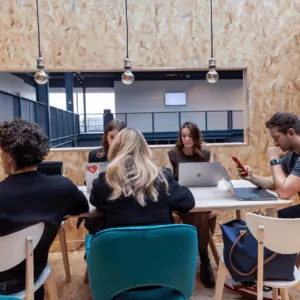 Espace de travail partagé moderne avec table, ordinateurs portables et personnes concentrées.