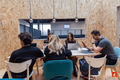 Espace de travail partagé moderne avec table, ordinateurs portables et personnes concentrées.