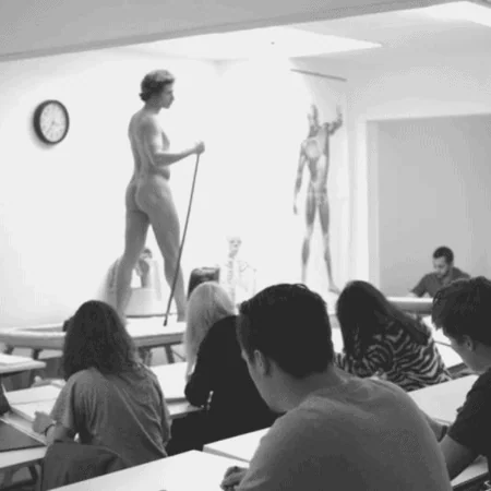 Modèle nu en pose dans atelier de dessin académique, étudiants réalisant croquis anatomiques.