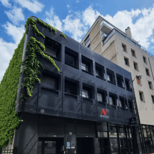 Façade urbaine moderne à grille noire, mur végétal, vitrine et ciel bleu.