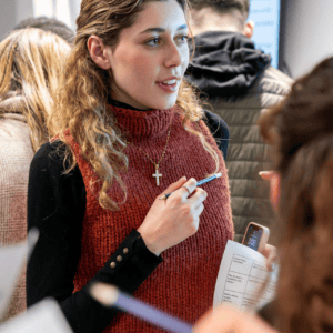 Femme prenant des notes en atelier avec stylo, smartphone et feuille de travail.
