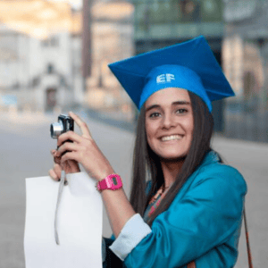 Femme diplômée souriante coiffée dune toque bleue, portrait urbain avec appareil photo.