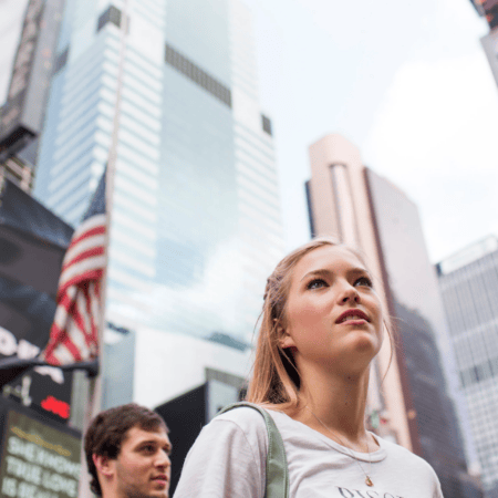 Jeune femme regardant les gratte-ciel en ville, drapeau américain et foule urbaine.