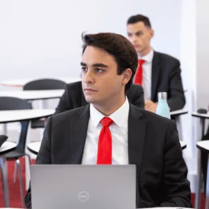 Jeune professionnel en costume et cravate rouge avec ordinateur portable en salle de formation.