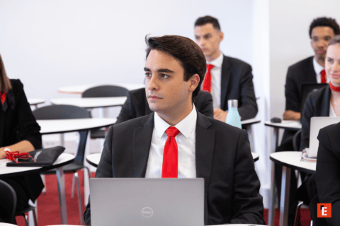 Jeune professionnel en costume et cravate rouge avec ordinateur portable en salle de formation.