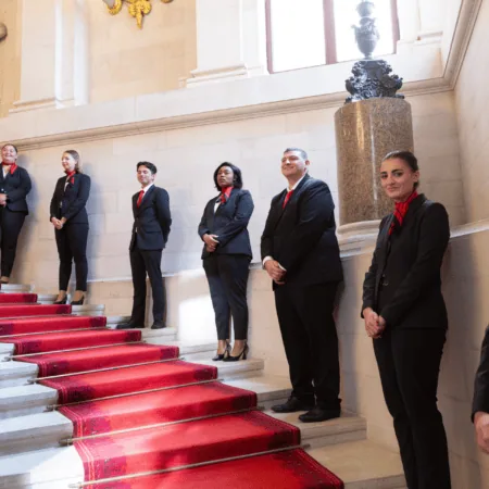 Groupe professionnel sur escalier à tapis rouge, intérieur historique, costumes et cravates rouges.