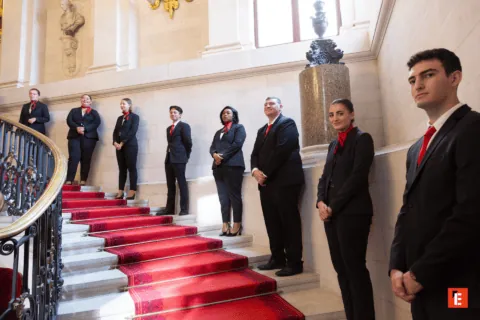 Groupe professionnel sur escalier à tapis rouge, intérieur historique, costumes et cravates rouges.