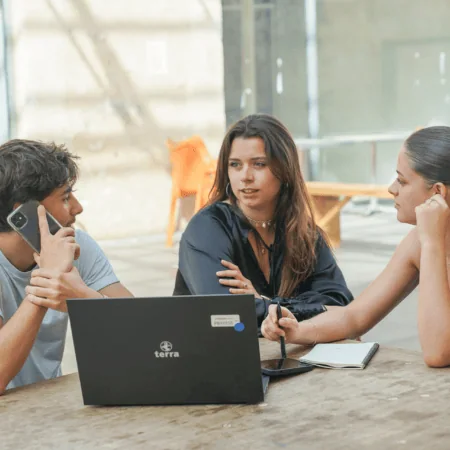 Trois jeunes en coworking autour dun ordinateur portable, réunion informelle, prise de notes.