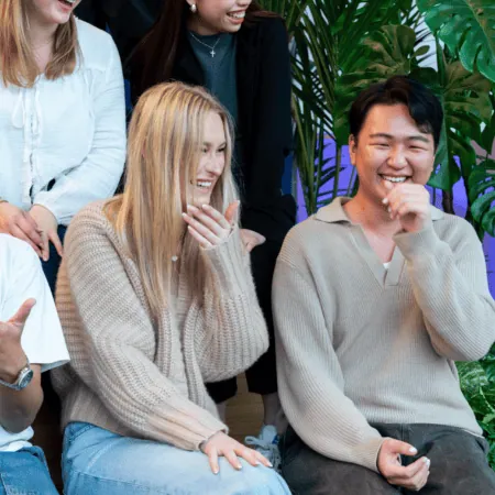 Groupe de jeunes adultes riant sur canapé, ambiance conviviale, plantes vertes en arrière-plan.