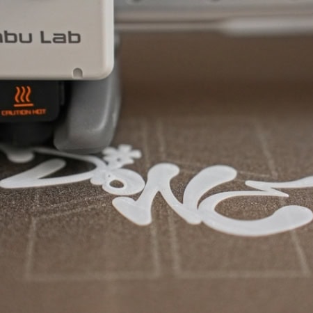 Impression 3D Bambu Lab, gros plan sur buse chaude extrudant du texte en plastique.