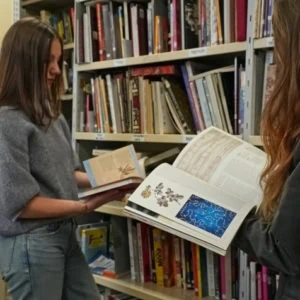 Deux lecteurs feuilletant des livres dans une bibliothèque aux rayonnages remplis.