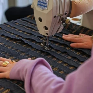 Machine à coudre Sewmaq cousant tissu rayé noir et or, mains dartisan guidant la couture.