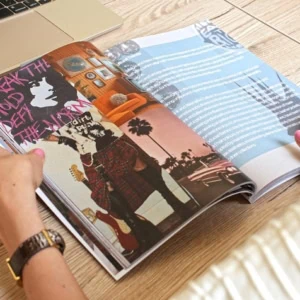 Magazine ouvert sur table en bois, collage guitare et design graphique, mains feuilletant.