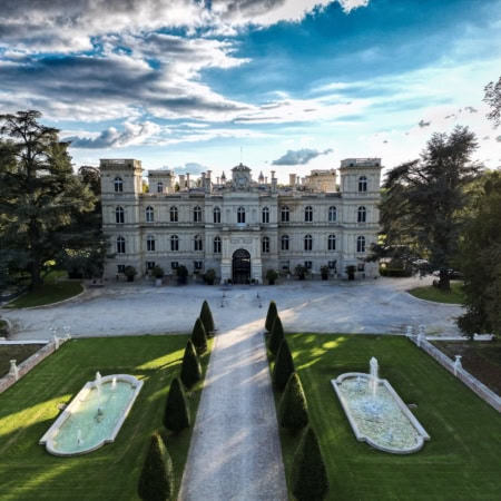 Manoir classique en pierre, allée centrée, bassins réfléchissants et fontaines dans jardins symétriques.