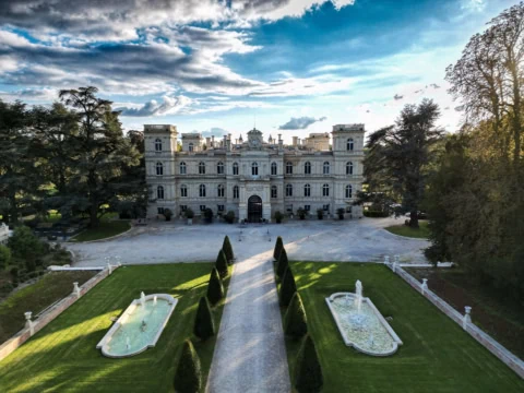 Manoir classique en pierre, allée centrée, bassins réfléchissants et fontaines dans jardins symétriques.