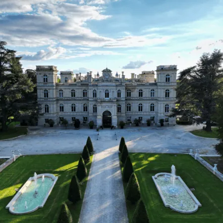 Manoir symétrique en pierre avec allée pavée, bassins réfléchissants et jardins formels.