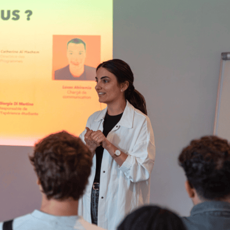 Oratrice féminine présentant une formation devant public, projection diapositive en arrière-plan.