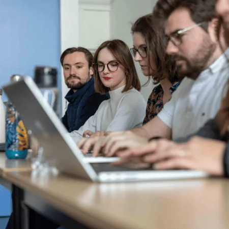 Participants en réunion déquipe autour dune table avec ordinateurs portables, collaboration en bureau.