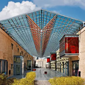 Passage piéton couvert en verrière métallique entre façades en pierre, perspective profonde.