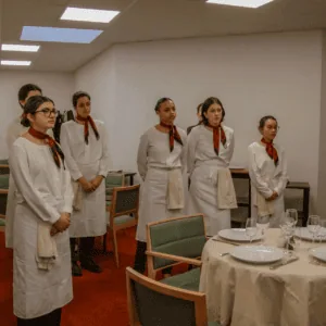Personnel de service en uniforme blanc en formation devant table dressée dans salle à manger.