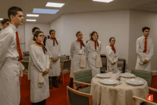 Personnel de service en uniforme blanc en formation devant table dressée dans salle à manger.