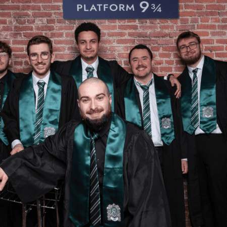 Photo de groupe de diplômés en robes et écharpes vertes devant Voie 9 3/4.