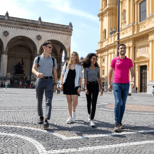 Groupe de jeunes marchant sur place historique pavée devant arcades et façade déglise ornée.