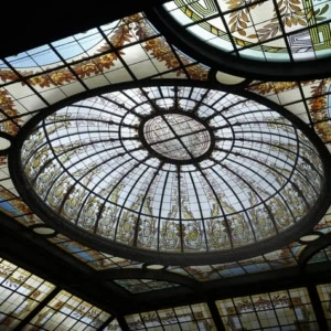 Plafond vitrail en dôme ovale, verrière à oculus, panneaux radiants et motifs floraux.