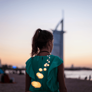 Femme de dos en robe verte sur plage au coucher de soleil, guirlande lumineuse scintillante.