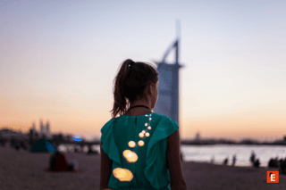 Femme de dos en robe verte sur plage au coucher de soleil, guirlande lumineuse scintillante.