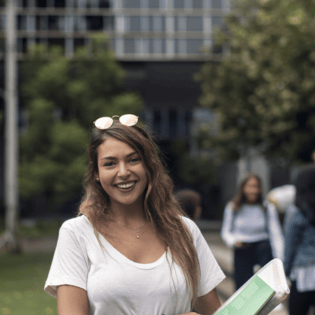 Portrait détudiante souriante sur campus, carnet vert et style décontracté.