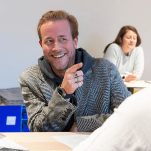 Portrait dhomme souriant en blazer et sweat, montre et bagues, discutant en réunion.