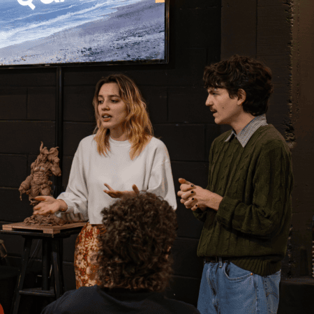 Présentation atelier de figurine fantastique devant public, sculpture exposée, écran océan et affiches.