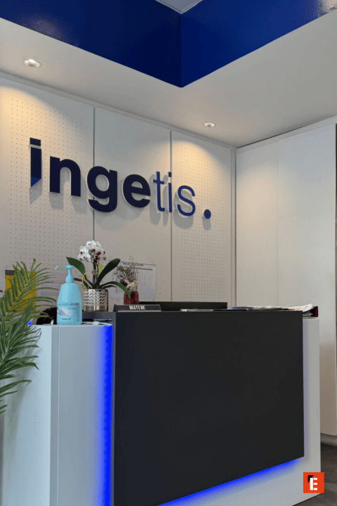 Réception moderne Ingetis avec logo bleu, comptoir minimaliste, éclairage LED et orchidée.