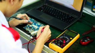 Réparation carte mère PC portable avec multimètre et sondes sur poste de travail.