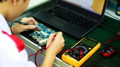 Réparation carte mère PC portable avec multimètre et sondes sur poste de travail.