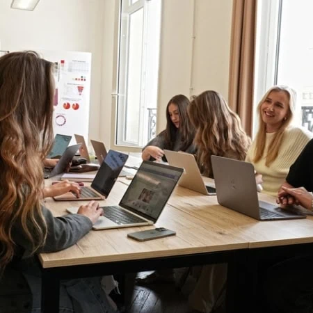Étudiants en réunion collaborative autour dune table en bois avec ordinateurs portables.