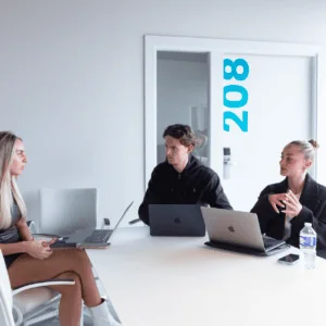 Réunion en salle 208 avec ordinateurs, participants concentrés et lumière naturelle.