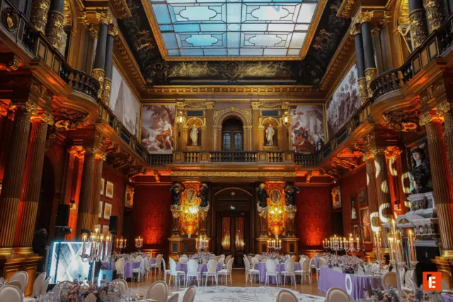 Salle de banquet luxueuse avec verrière, colonnes corinthiennes, tables élégantes et lustres.