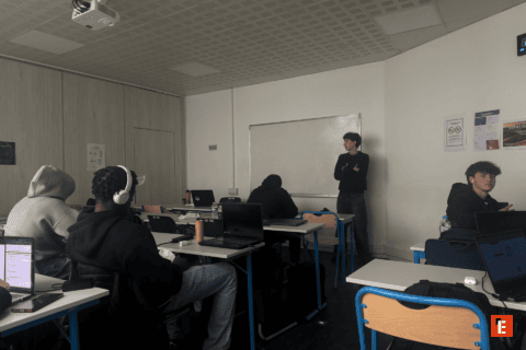 Salle de cours avec étudiants et ordinateurs portables, tableau blanc, casques et ambiance studieuse.