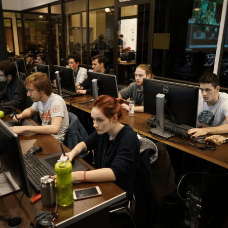 Salle informatique : étudiants concentrés sur ordinateurs et tablettes graphiques, atelier créatif nocturne.