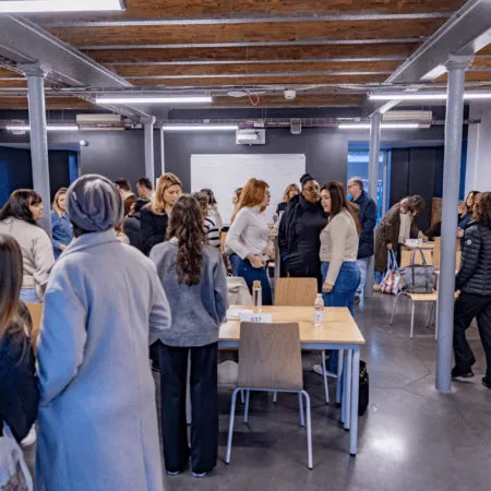 Salle de réunion industrielle collaborative avec participants, tables, chaises, projecteur et plafond apparent.
