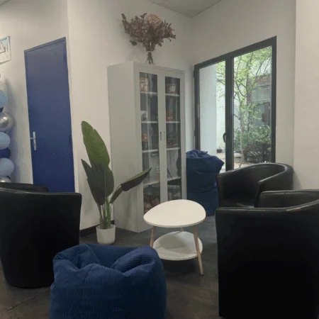 Salon dattente moderne bleu avec fauteuils noirs, table ronde et baie vitrée.