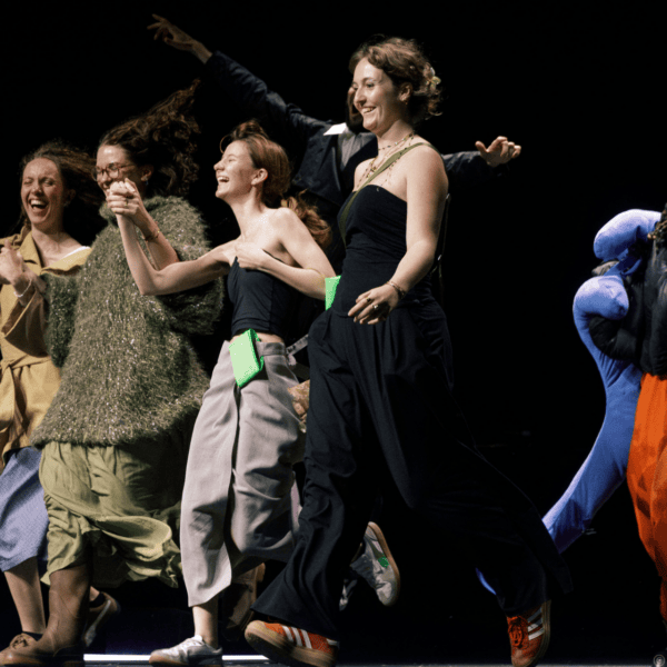 Groupe dartistes en spectacle dansant sur scène, costumes colorés, lumière contrastée, joie et mouvement.
